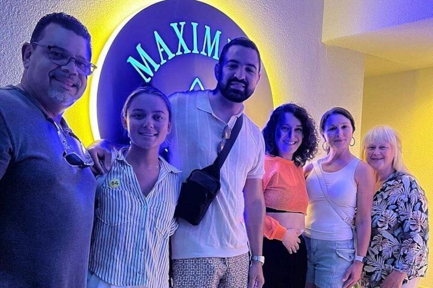 A group of people posing in front of a neon sign with the word 'MAXIMUS' on it. 5