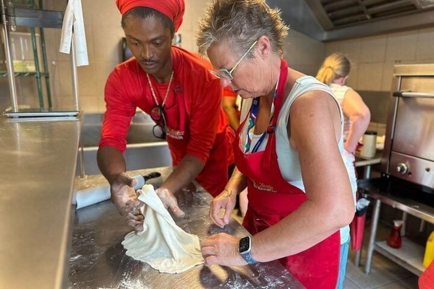 Dos personas en una cocina preparando comida, con un mostrador de acero inoxidable y un horno grande al fondo. 1