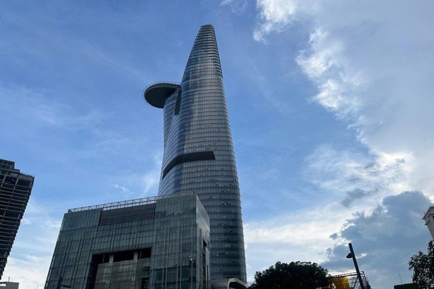 A tall, modern skyscraper with a unique tapered design, surrounded by other buildings and a partly cloudy sky. 2