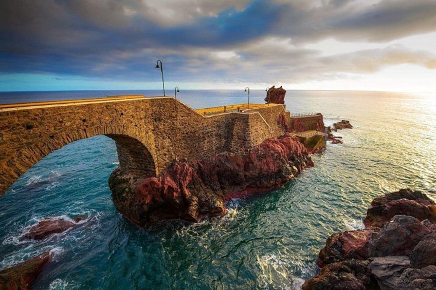 A stone bridge over a rocky coastline with waves crashing below. 3
