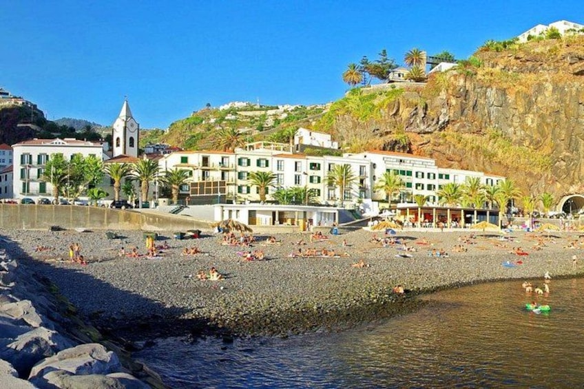 A beach with people sunbathing, a rocky shoreline, and buildings in the background. 2
