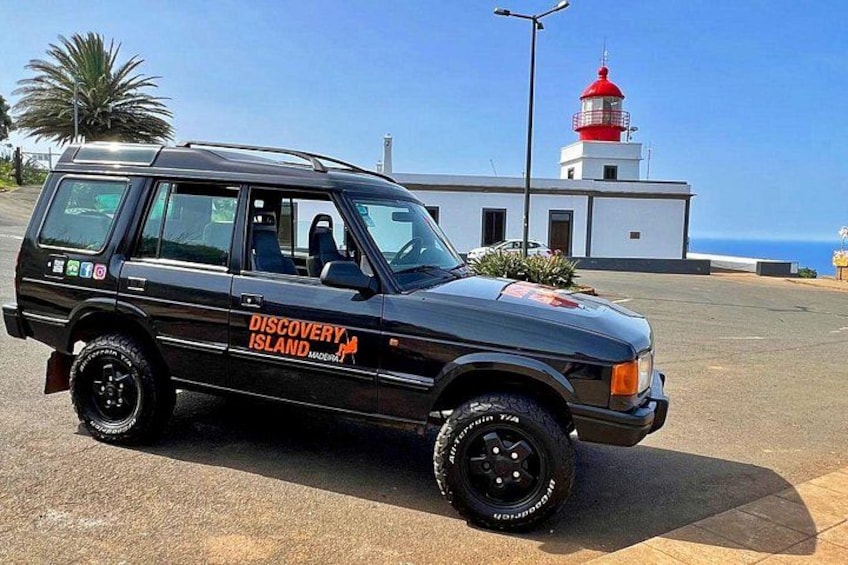 A black Discovery Island vehicle parked in front of a white building with a red lighthouse. 1