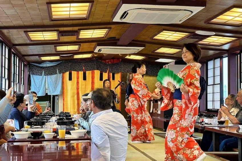 A traditional Japanese setting with people in kimonos, a wooden table with dishes, and a stage with a microphone. 2