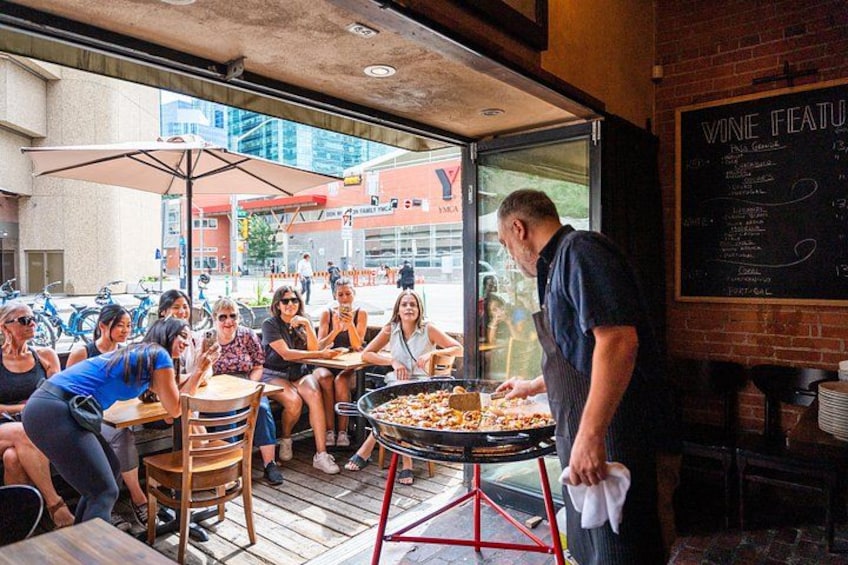 An outdoor dining area with a grill, people eating, and a menu board. 4