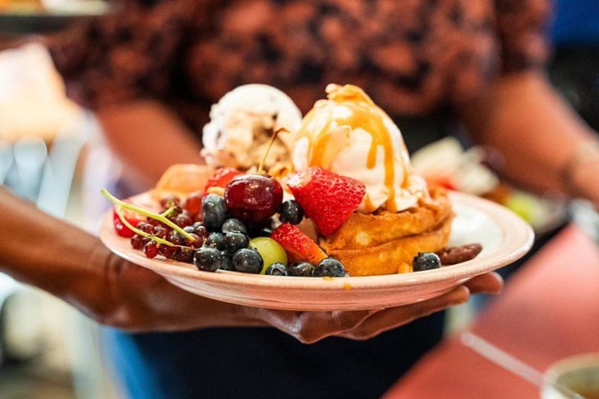 A person holding a plate with pancakes, ice cream, and assorted berries. 2