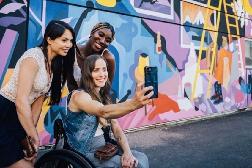 Tre personer som tar en selfie framför en färgstark väggmålning. 4