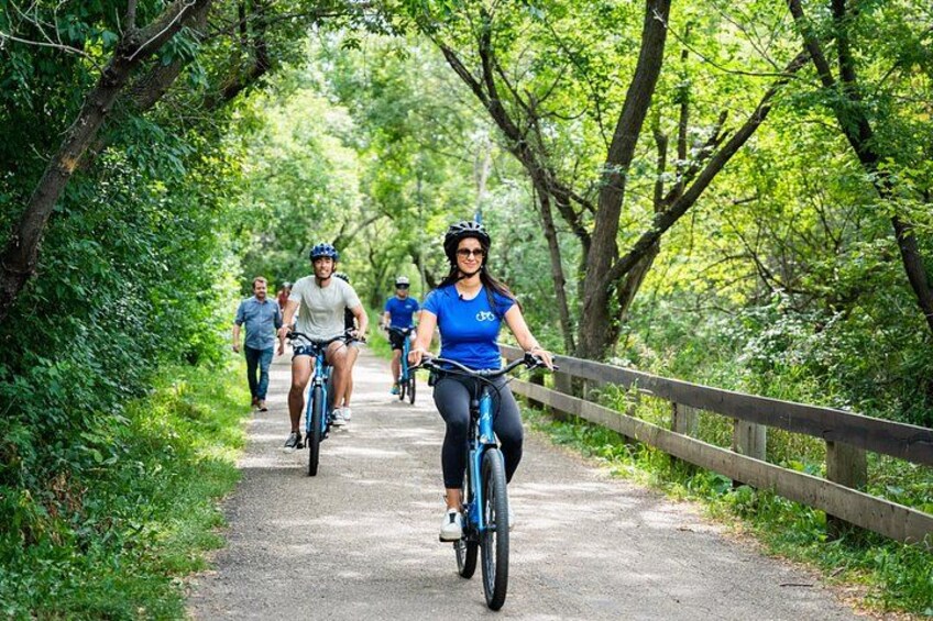 Eine Radfahrer-Gruppe auf einem asphaltierten Weg, umgeben von Bäumen. 2