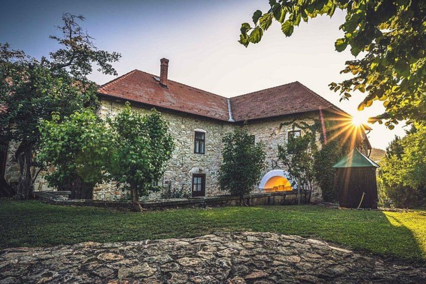 A stone building with a red roof, surrounded by trees and a stone pathway. 1