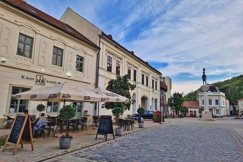 Une rue pavée bordée de cafés, de terrasses et d’une statue. 3
