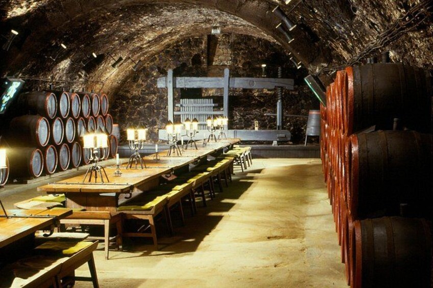 Une cave à vin avec des tables en bois, des barriques et un plafond voûté. 1