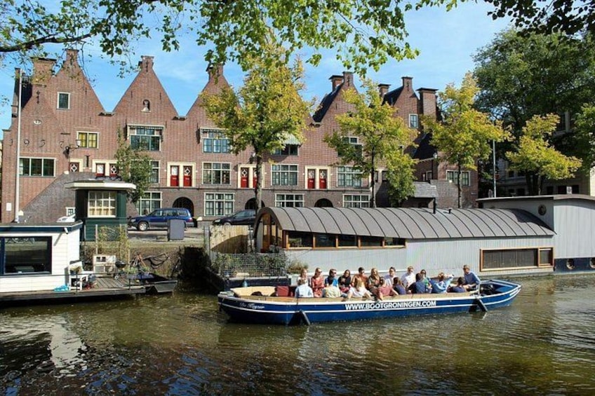 Ein Kanal mit einem Boot, das Personen befördert, ein rotes Backsteinhaus und ein Baum. 3