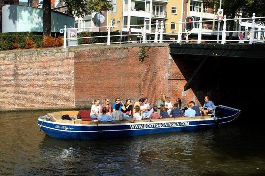 Ein blaues Boot mit Personen, das an einem Kanal vor einer Backsteinmauer und einer Brücke liegt. 2