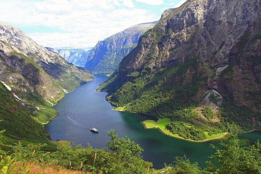 Et fjord omgivet af stejle klipper, en båd på vandet og en lille ø med grønt. 4