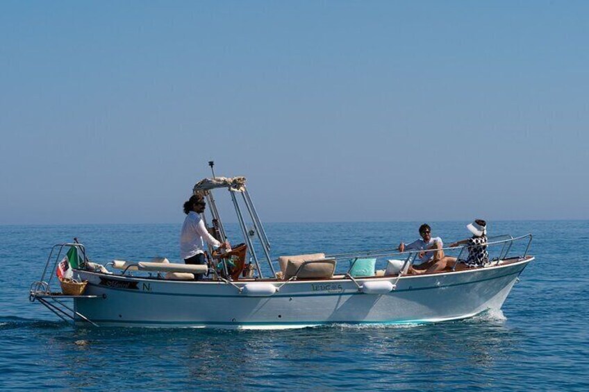 A small motorboat with two people on board, one steering and one sitting, on calm blue water. 1