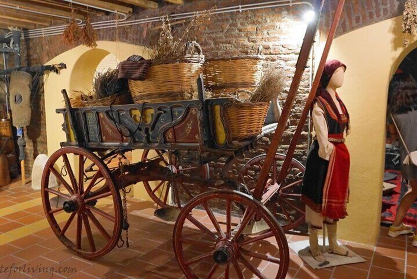 A vintage wooden cart with red wheels, a mannequin dressed in traditional attire, and a rustic interior with stone walls and a tiled floor. 3