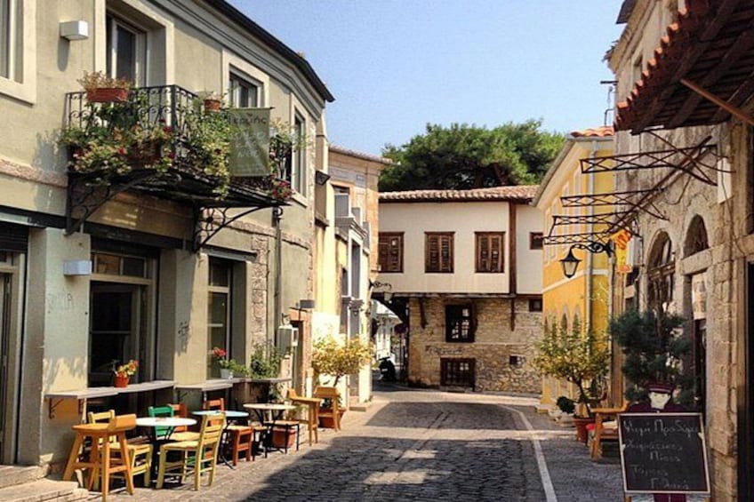 A cobblestone street with outdoor seating, buildings with balconies, and a clear sky. 1