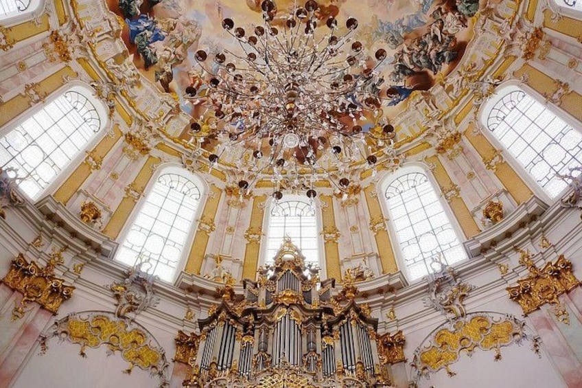 A grand interior with a large ornate chandelier, gold accents, and a central organ. 2