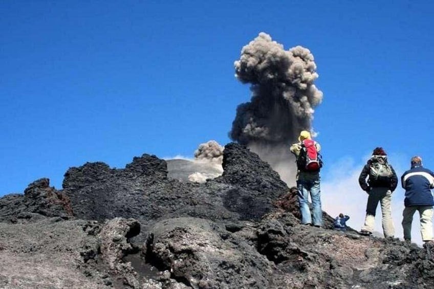 A volcanic eruption with smoke and ash, rocky terrain, and people observing the event. 1