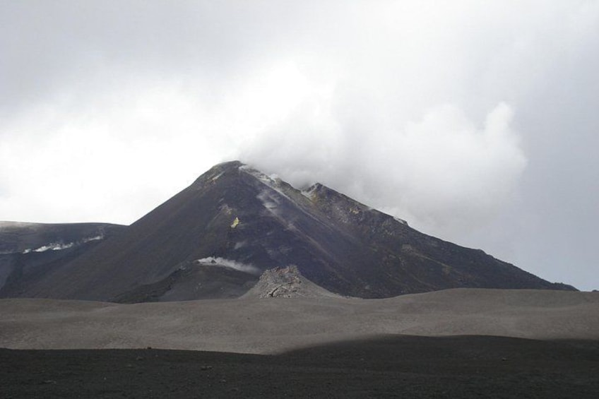 A mountain with a snow-capped peak, a flat plain in the foreground, and a cloudy sky. 2
