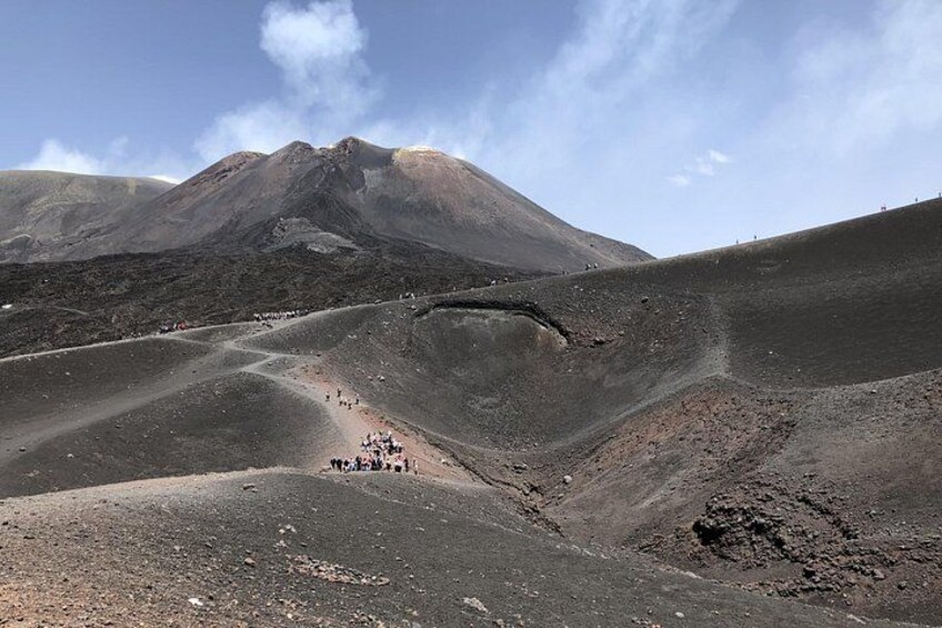 A volcanic landscape with a crater, a group of people, and a mountain in the background. 4
