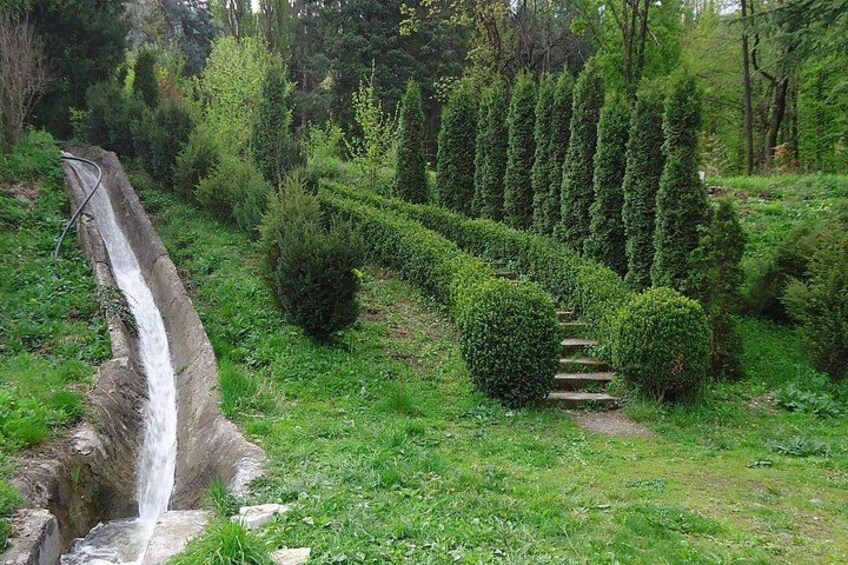 A waterfall, a stone staircase, and neatly trimmed hedges in a park. 4