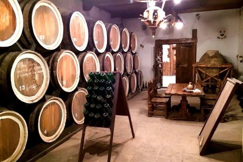 A cellar with wooden barrels stacked against the wall, a wooden table, and a rustic chandelier. 1