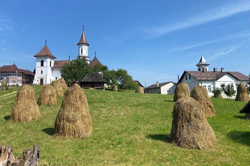 Un paysage rural avec des bottes de foin, une église dotée d’un clocher et des maisons traditionnelles. 2
