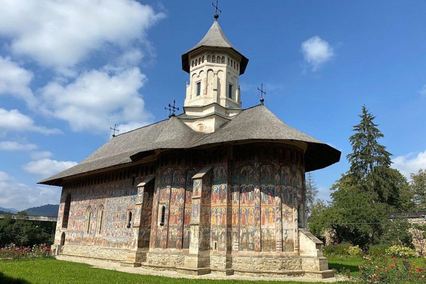 Une église dotée d’un dôme et d’un clocher, entourée de verdure et surplombée d’un ciel dégagé. 1