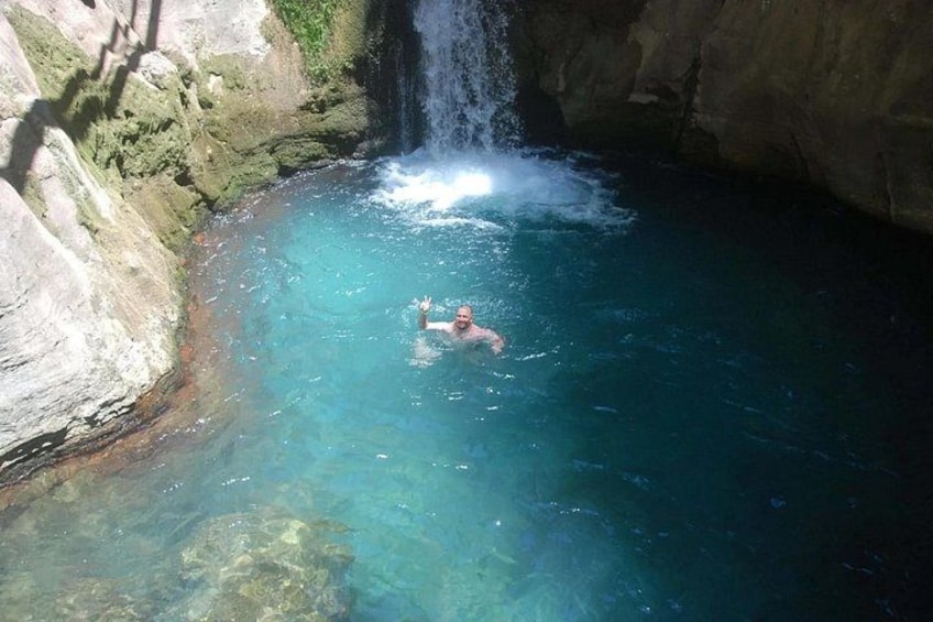 Une personne nage dans une piscine à l’eau claire et bleue, avec une cascade en arrière-plan. 1