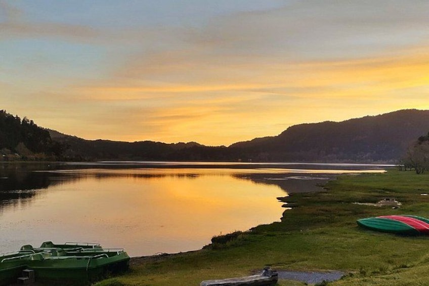 A calm lake at sunset with boats on the shore and hills in the background. 3