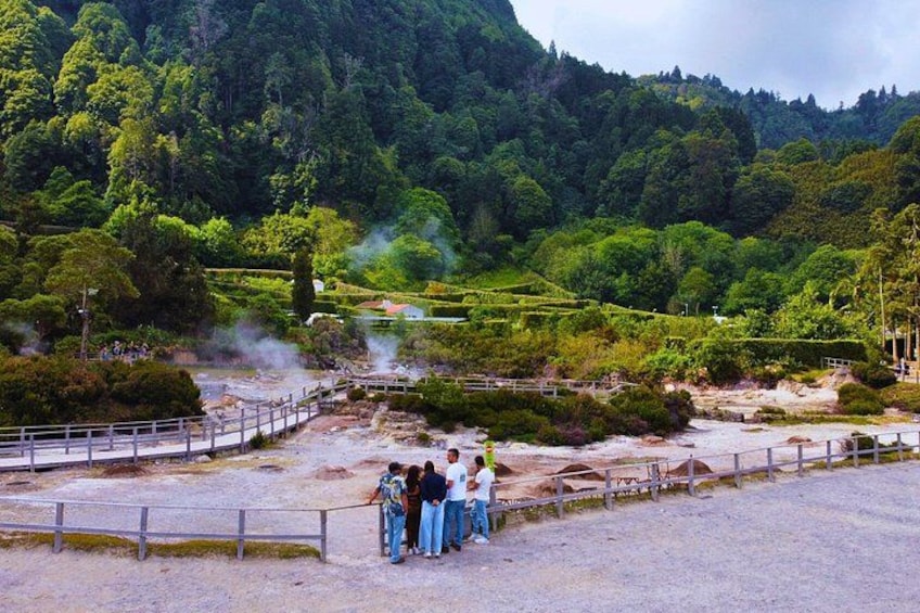 A geothermal area with steam vents, a wooden bridge, and a group of people observing the landscape. 4