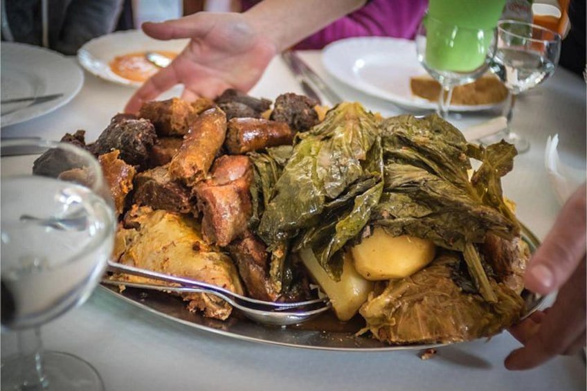 Una bandeja grande con carnes asadas y verduras, incluyendo un pollo entero y hojas verdes, servida en una mesa de comedor. 3