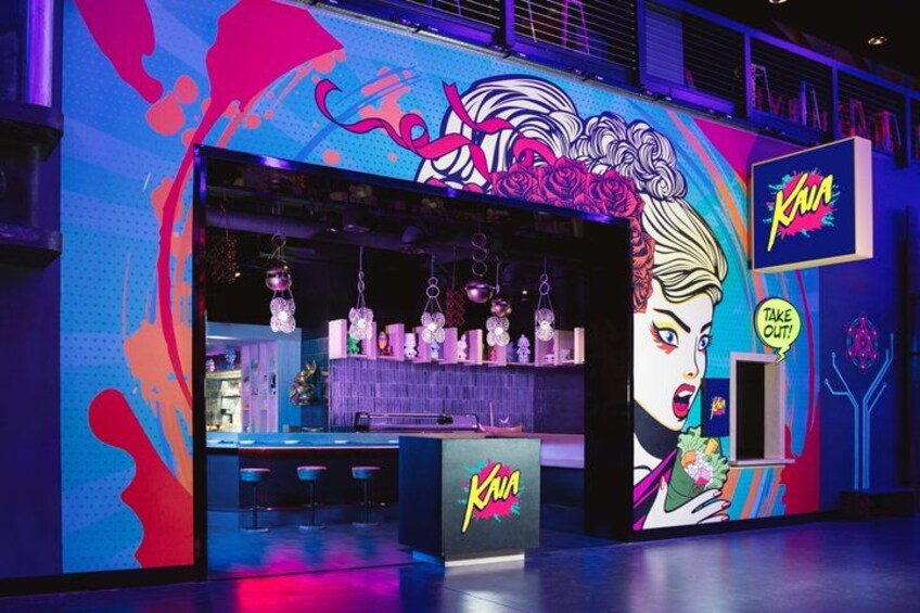 Ein lebhaft gestalteter Ladenfront mit einer großen Wandmalerei, hängenden Dekorationen und einem Neonzeichen. 2