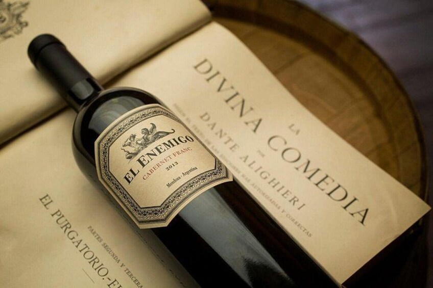 A bottle of El Enemigo wine with a label, placed on top of a book titled 'Divina Comedia.' 1