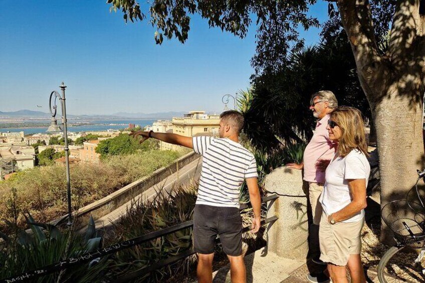 Un grupo de personas de pie sobre un muro de piedra contemplando un paisaje urbano bajo un cielo despejado. 2