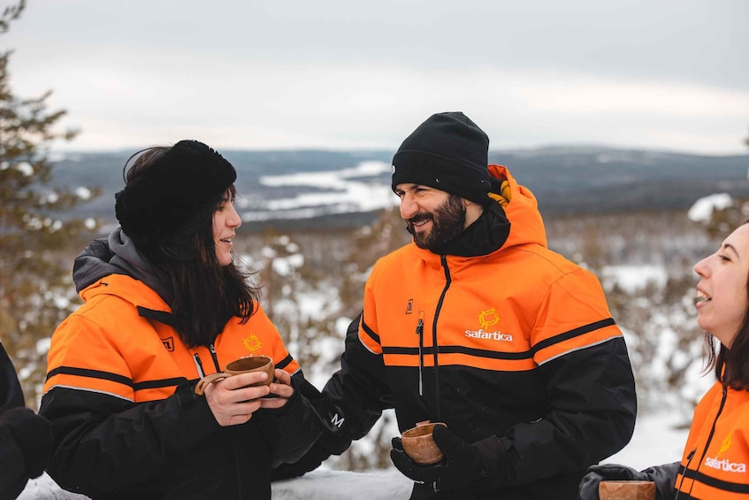 Two people in safari jackets holding small bowls, standing outdoors with a snowy landscape in the background. 3