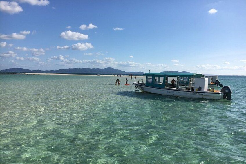 A boat on clear turquoise water with a beach and mountains in the background. 2