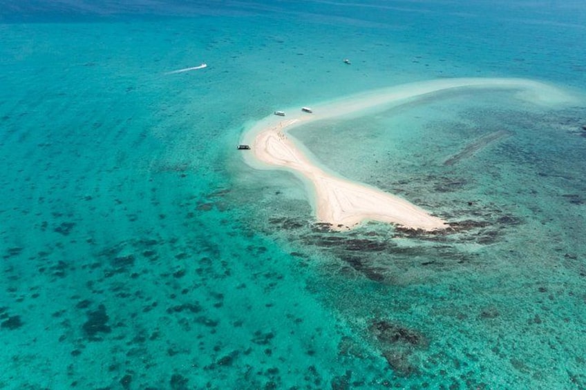 Eine Luftaufnahme eines Strandes mit klarem türkisblauem Wasser, einem sandigen Ufer und einem Boot in der Ferne. 4