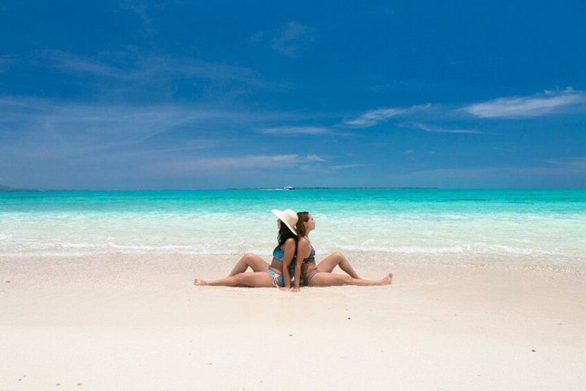 Dos personas sentadas en una playa con cielo azul despejado y mar turquesa. 4