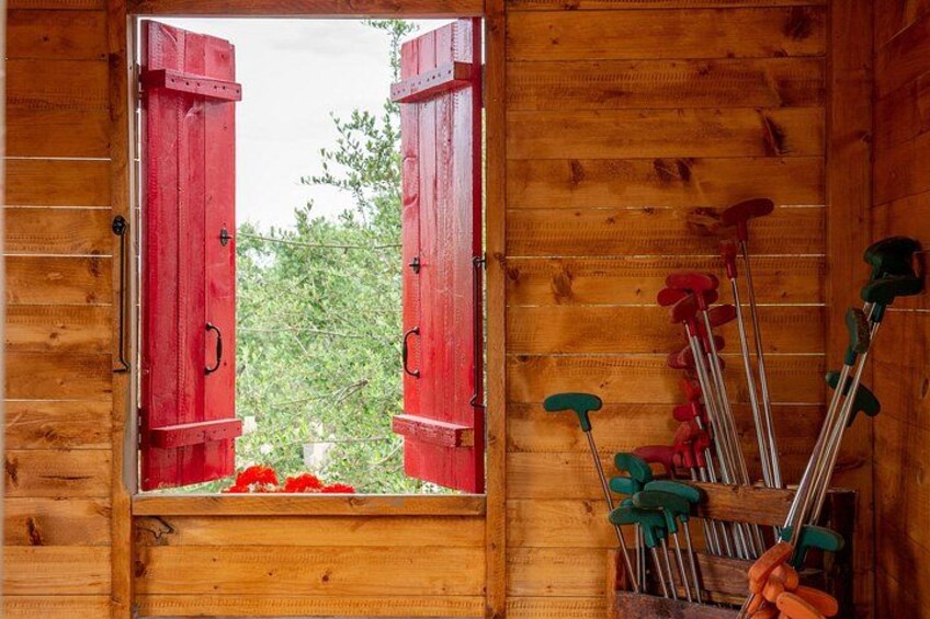 A wooden cabin with a window open, revealing a garden with red flowers and a pile of ski poles. 2