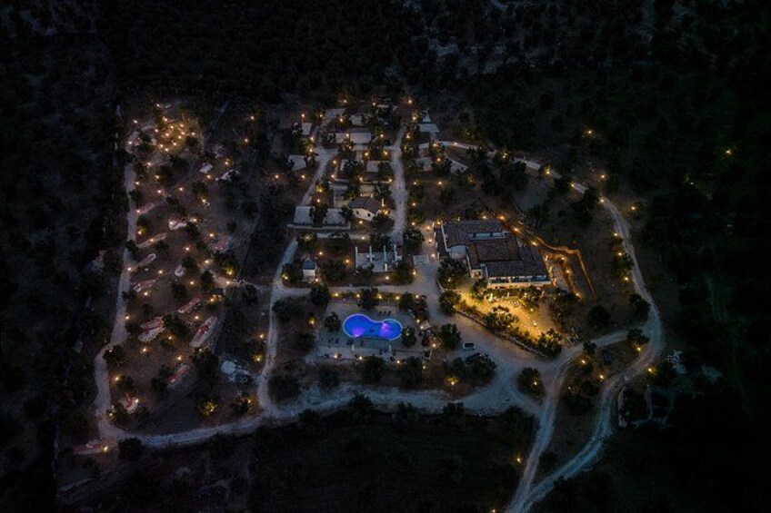 An aerial view of a well-lit resort area with multiple buildings, a swimming pool, and surrounding pathways. 4
