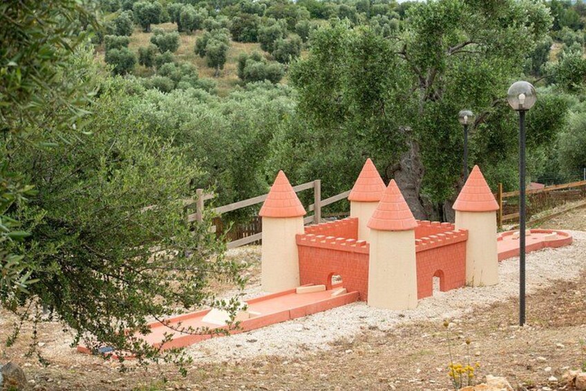A castle-like structure with red roofs and beige walls, surrounded by a fence and trees. 5