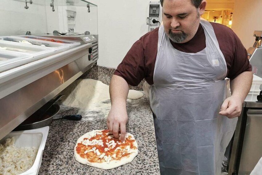 A person preparing food, possibly making pizza, in a kitchen with a granite countertop and stainless steel appliances. 3