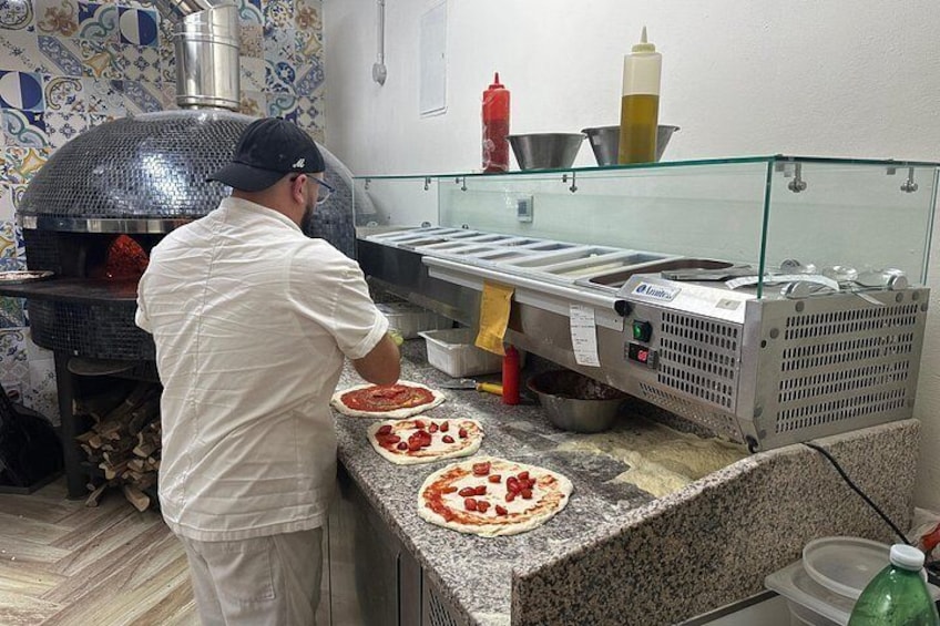 A chef preparing pizzas in a kitchen with a brick oven and a marble countertop. 2