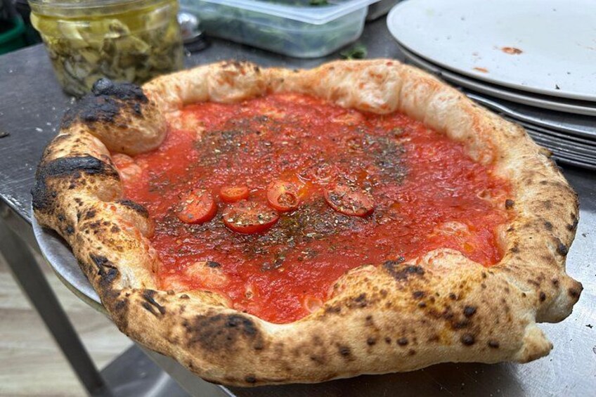 Pizza mit knusprigem, leicht verbranntem Rand, Tomatensauce und Tomatenscheiben auf einer Metallplatte. 1