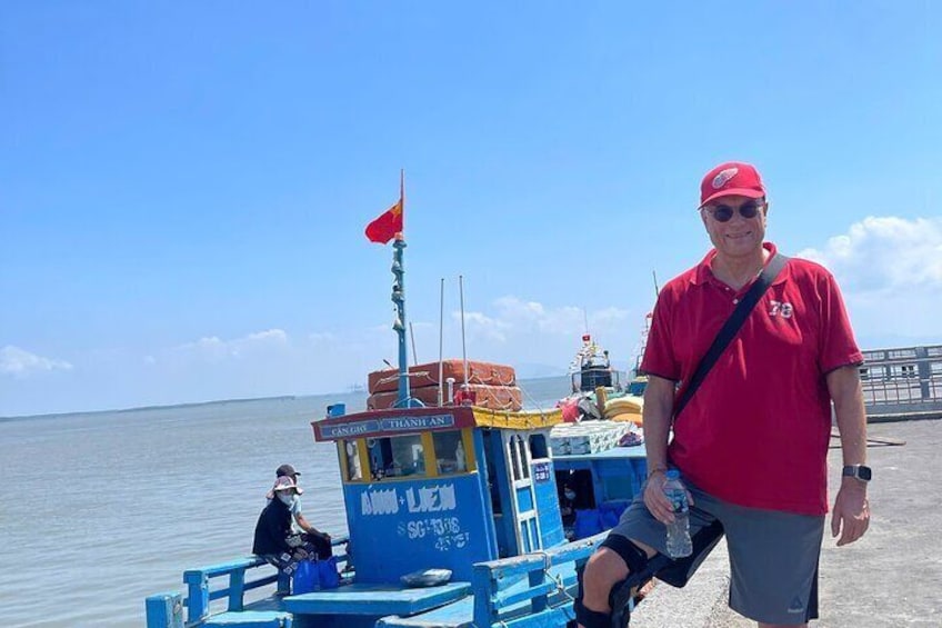 A man in a red shirt standing on a dock with a boat in the background. 2
