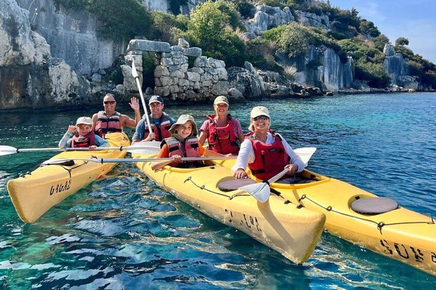 Een groep mensen kajakt op een heldere dag, met rotsachtige kliffen en rustig water op de achtergrond. 1