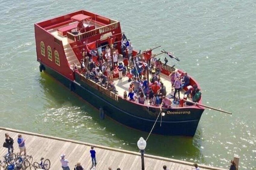 Un barco rojo y azul llamado 'Boomerana' con gente a bordo, atracado en un muelle de madera. 2