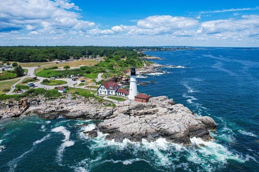 A lighthouse on a rocky outcrop with a coastal road and greenery in the background. 1