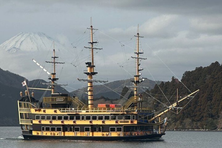 A large, multi-decked ship with multiple masts and flags, sailing on a body of water with a mountainous backdrop. 2